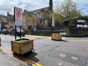  Doing R Bit retractable barrier system which is housed in a sustainable timber roadside planters either side of a road with school building in background