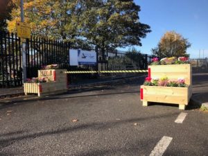  Doing R Bit retractable barrier system which is housed in a sustainable timber roadside planters either side of a road with school fence and trees in background
