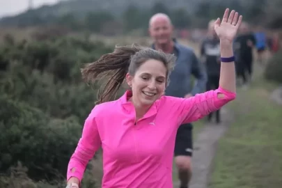 Heidi Pearson running, wearing bright pink top and waving.