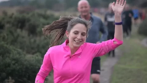 Heidi Pearson running, wearing bright pink top and waving.