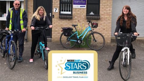 Three Brightwayz team members gather on bikes outside the Brightwayz office. Modeshift STARS Gold accreditation logo in the foreground.