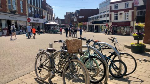 Four bikes parked in bike parking station in Kettering Town Centre, high street in background with shops and people walking.
