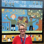 Image shows Beverly Furbur from The Ridge Primary school smiling infront of a sign wearing a red top