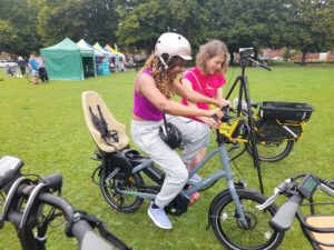 Caz Conneller helps woman trialing an e-bike at pilot event. Green field with tents and people in the background. 