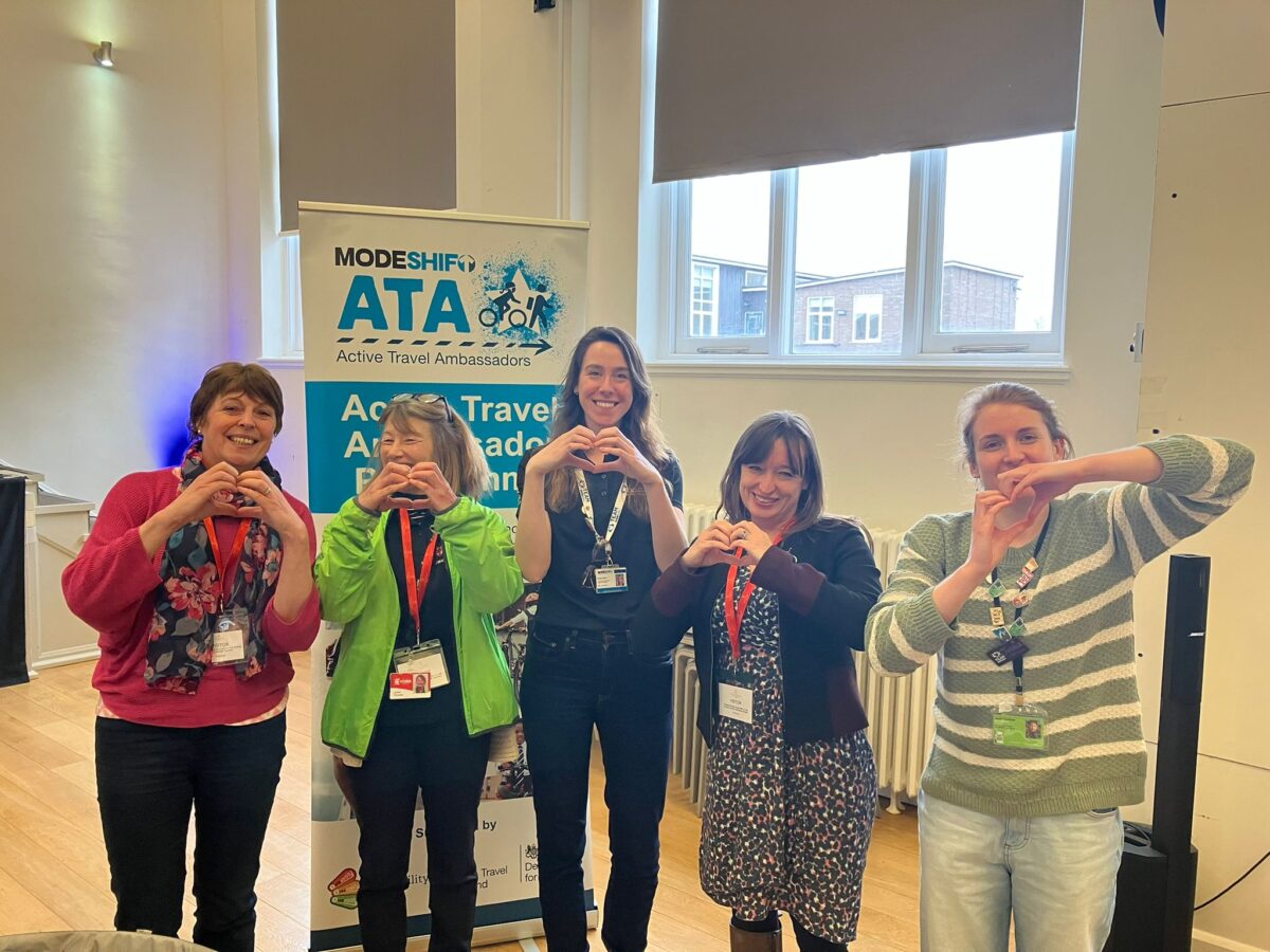 Five women stand making a heart shape with their hands for International Women's Day