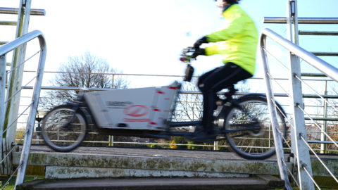 Cargo bike in motion - ridden by person in yellow high viz jacket and wearing a cycling helmet.