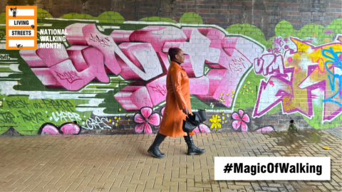 Person in motion. Person wearing orange dress walks past a wall of colorful graffiti. Text reads: #MagicofWalking