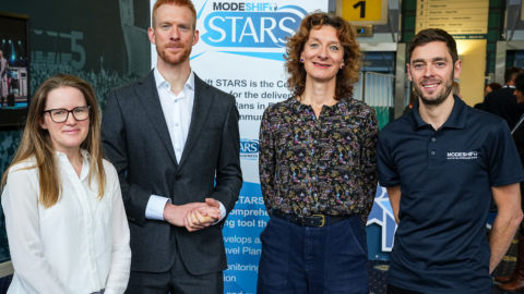 Four people stand in front of Modeshift STARS display stand smiling.
