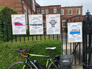 Posters on school railings, school in background. Bike propped up against railing.