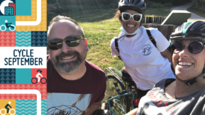 Three people smile at the camera wearing sunglasses. The two on the right wear cycle helmets. Text reads. Cycle September.