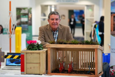 Man smiles at camera, he leans on a wooden crate.