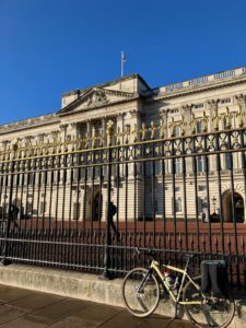 Bicycle in propped up on railings outside a large grand white building with large windows, ornate columns and a flag pole. 