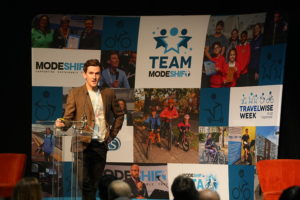 Man stands at lectern speaking to audience at the Modeshift Convention.