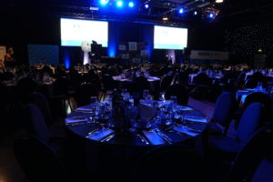 A spacious dining room featuring elegantly arranged tables and chairs prepared for a formal dinner event.