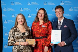 Three people stand together holding certificate and award trophy.