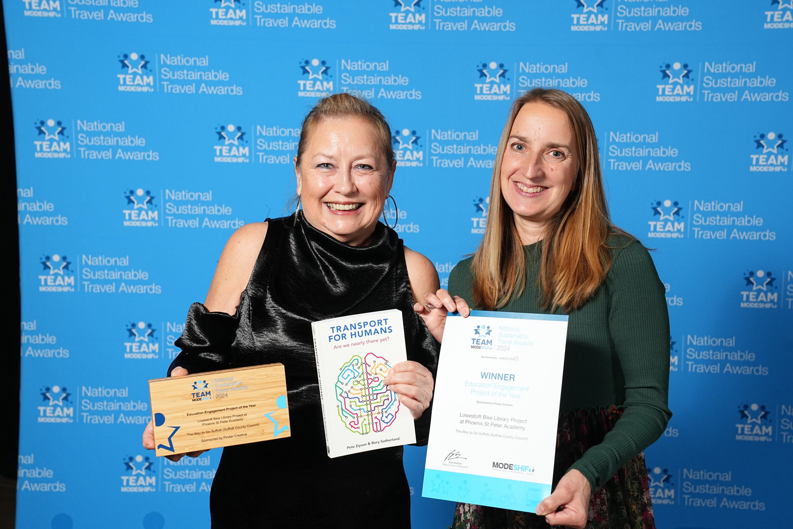 Two women stand side by side. They hold a certificate and award trophy.