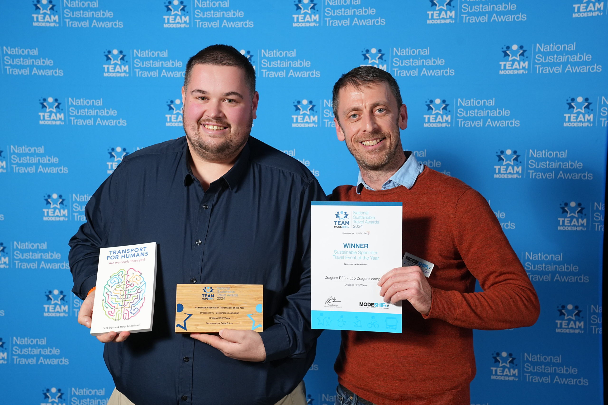 Two men stand together, holding their awards high at the national sustainable travel awards.