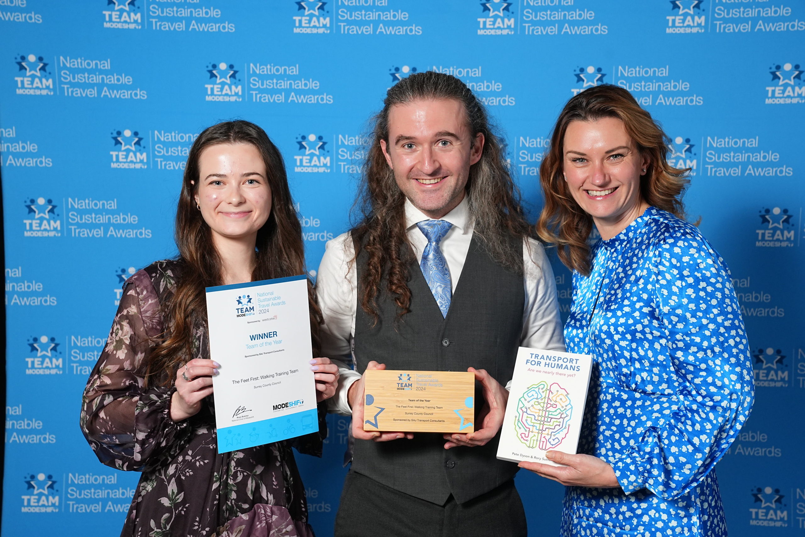 Three people stand together. Man in the middle with woman either side. They are holding their awards high at the national sustainable travel awards.