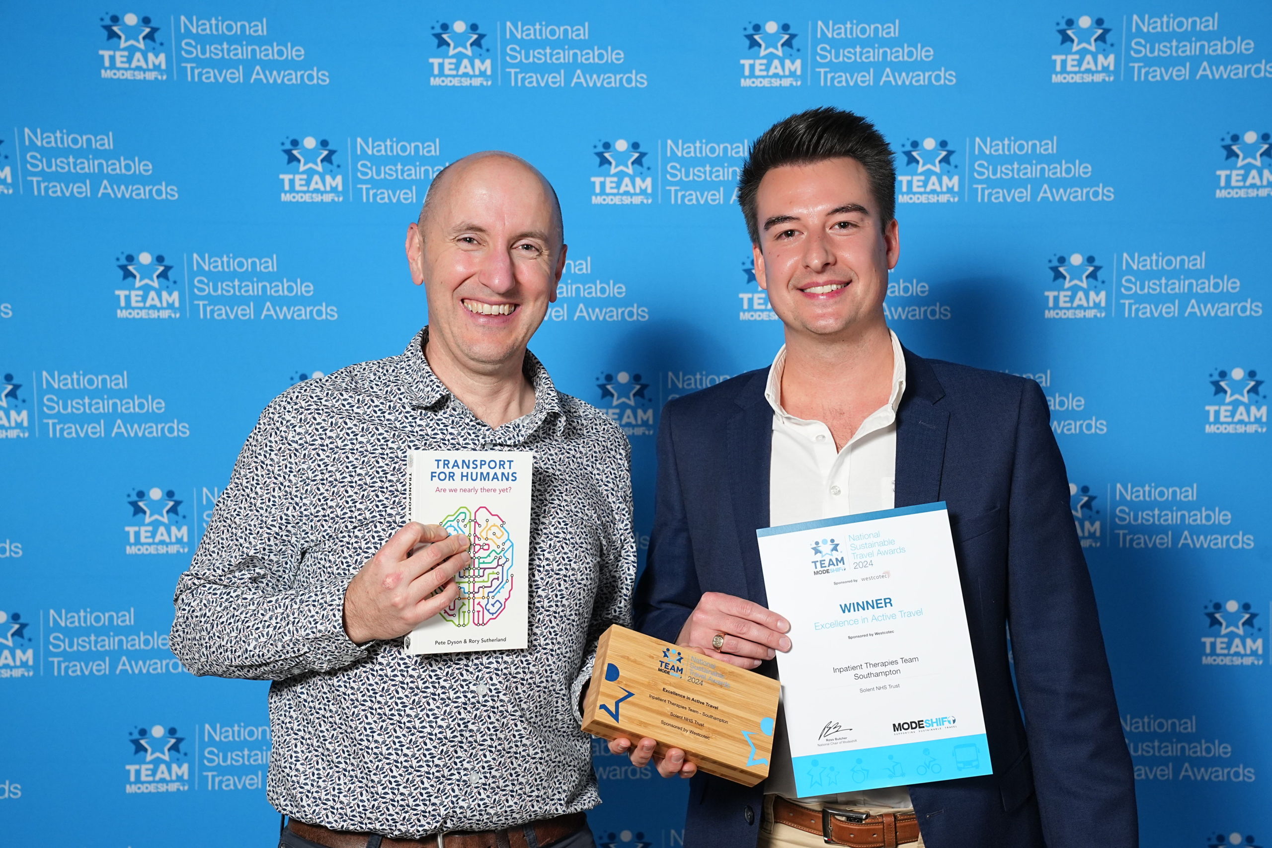 Two men stand together, holding their awards high at the national sustainable travel awards, symbolising their success and recognition.