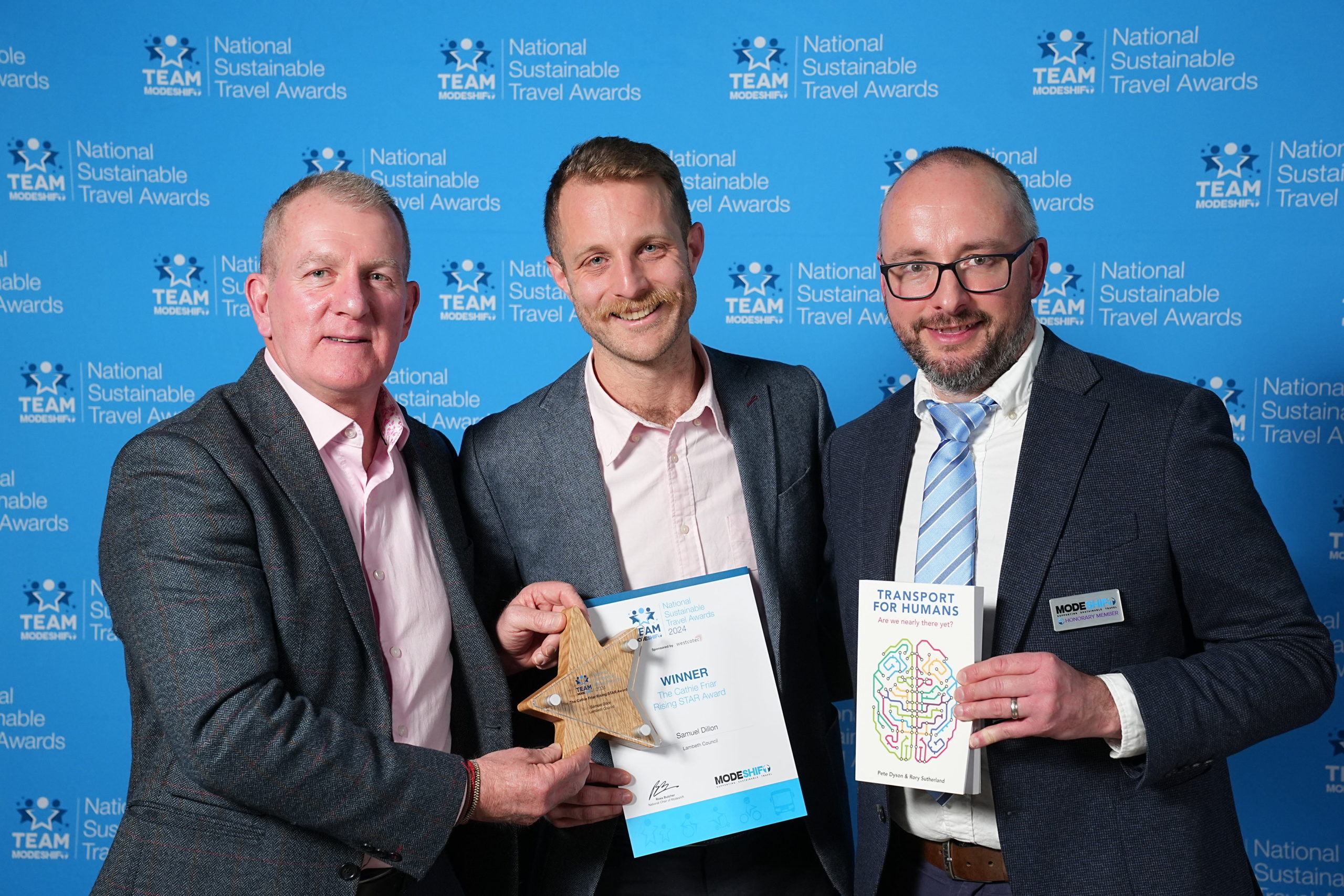 Three men stand together. holding their awards high at the national sustainable travel awards.