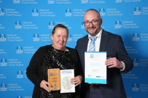 A man and woman stand together, holding their awards high at the national sustainable travel awards