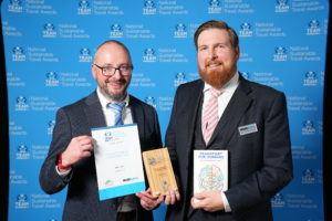 Two men stand together, holding their awards high at the national sustainable travel awards.