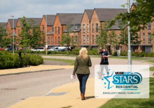 Two people walking down a paved residential street with houses and cars in the background. Greenery lines the street. Modeshift STARS Residential logo in teh bottom right corner. Text reads: 'Excellent Travel Plan 2024'.