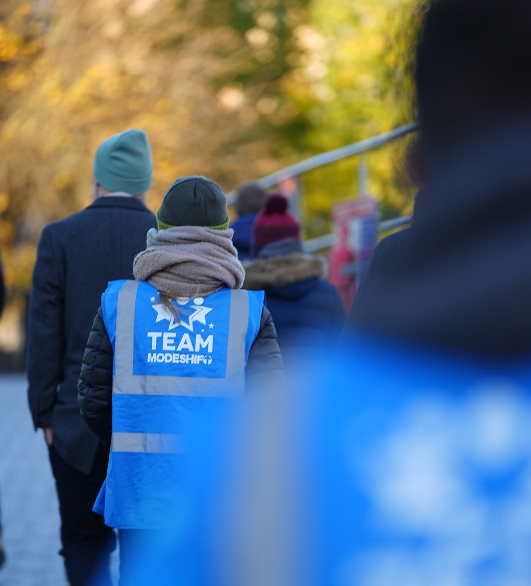 A group of people walking wrapped up in winter clothes, some wearing Team Modeshift blue high vis vests