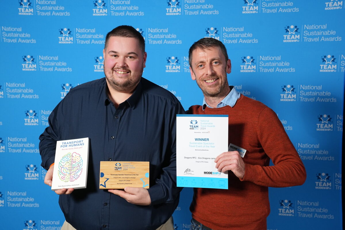 Two men smile at the camera, each holding a certificate and award.