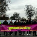 A diverse group of individuals stands in a parking lot, proudly holding a large banner together.