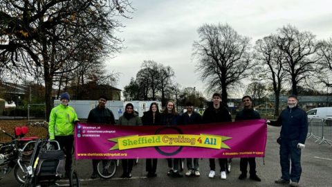 A diverse group of individuals stands in a parking lot, proudly holding a large banner together.