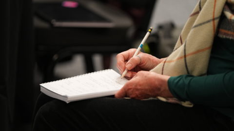 Close up image of woman's hands as she holds a pen to write on a note pad.