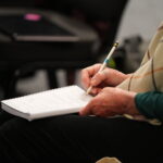 Close up image of woman's hands as she holds a pen to write on a note pad.