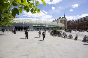 People walking outside the entrance to Kings Cross Station London. Bikes parked in racks in the foreground.