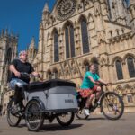 Image credit: Active Travel England. Two people cycle past York Minster. Person in the bottom left is peddling a Cargo Bike.