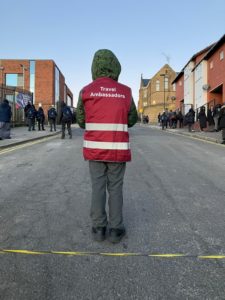 Child stands in closed School Street, back to the camera and wearing high viz jacket. Text on the jacket reads: 'Travel Ambassadors'. 