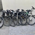 A row of seven black bikes are lined up against a wall. Seized modified bikes, credit: City of London Police
