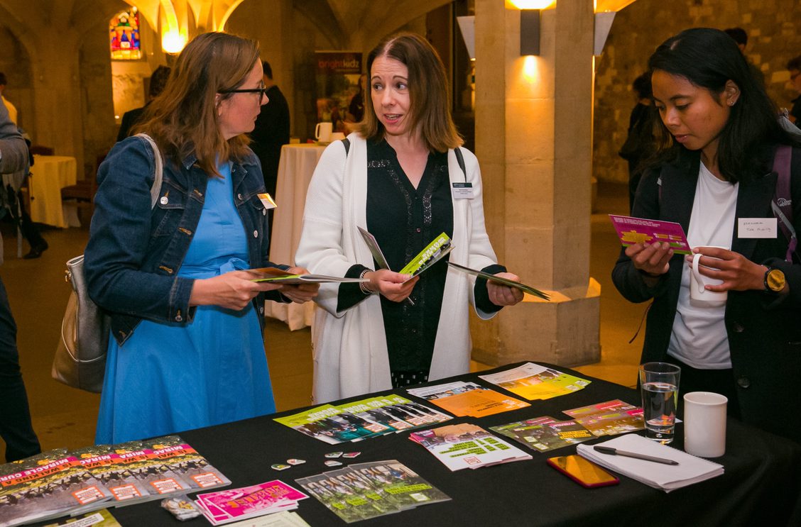 Three women at an Exhibition stand, reading various colourful leaflets