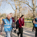 A group of people walking on a tree lined path. Smiling and in conversation.