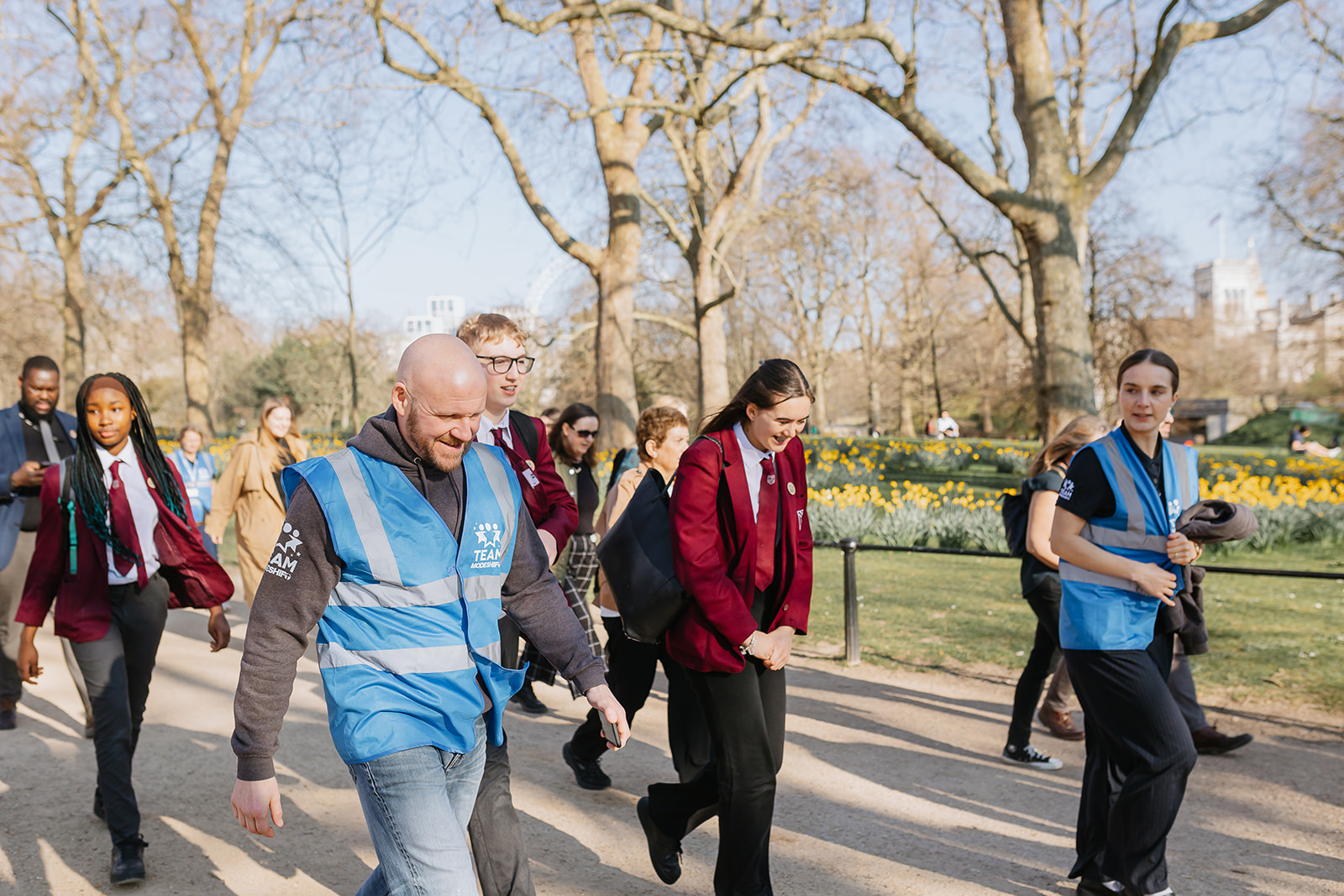 A group of people walking on a tree lined path. Smiling and in conversation.