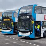 Multiple Stagecoach double-decker buses are lined up outside Connell Co-op College, ready for service. The destination signs display various matchday routes such as MC4 to Heald Green and MC12 to Wythenshawe. A driver in a high-visibility jacket stands at the door of one bus as passengers are visible seated inside.