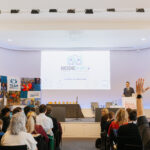 Audience members raise hands during a presentation at the ModeShift National STARS Summit in a modern conference hall.