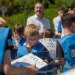 Children wearing blue vests labeled 'Active Travel Inspectors' reviewing clipboards outdoors during a group activity. How Active Travel Inspectors Support TfL's Walking and Wheeling Action Plan