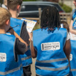A group of children photographed from behind, wearing blue high viz vests with the Active Travel Inspectors logo on