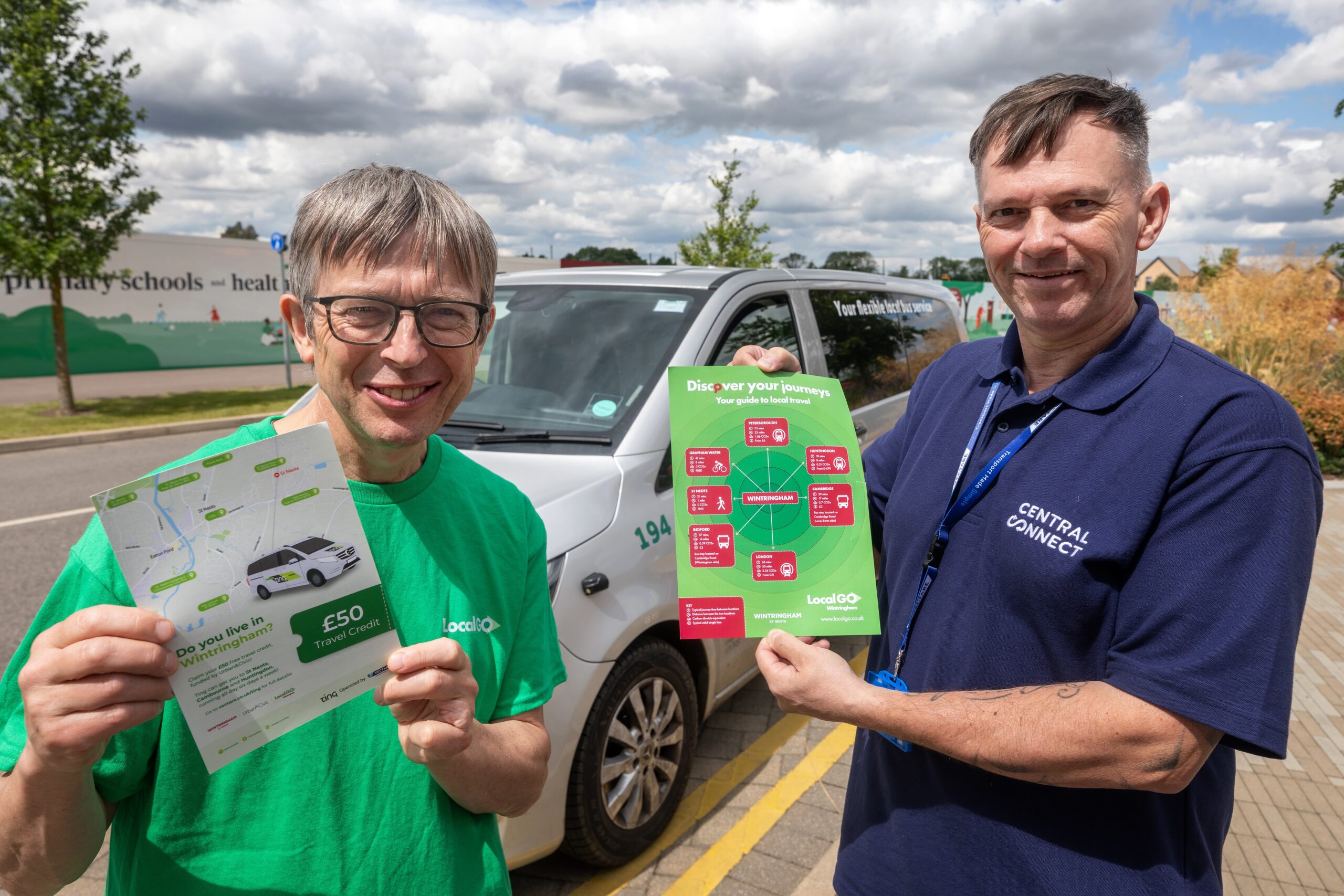 Two people stand outdoors holding LocalGo travel brochures in front of a white vehicle with LocalGo branding.