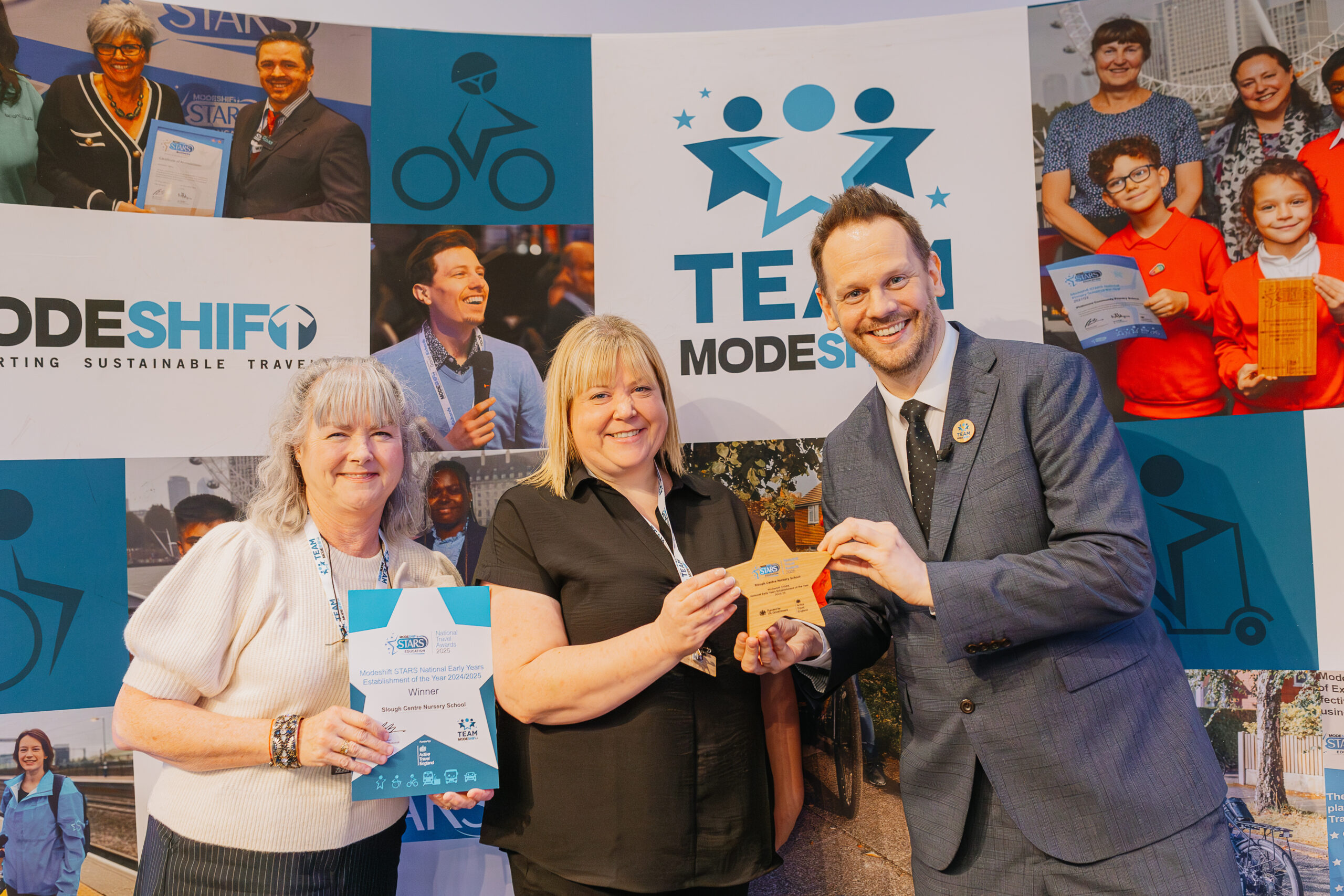 Three people smile, posing with Star shaped award. Modeshift display stand in the background.