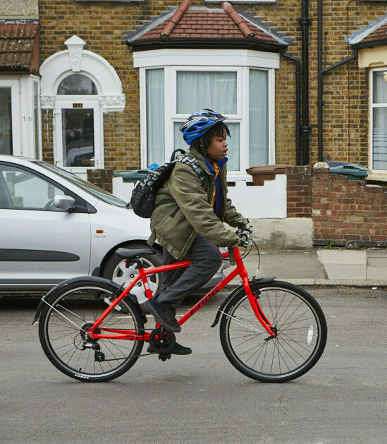 Child cycles down a residential street on a red bike. Wears green winter coat and blue helmet.