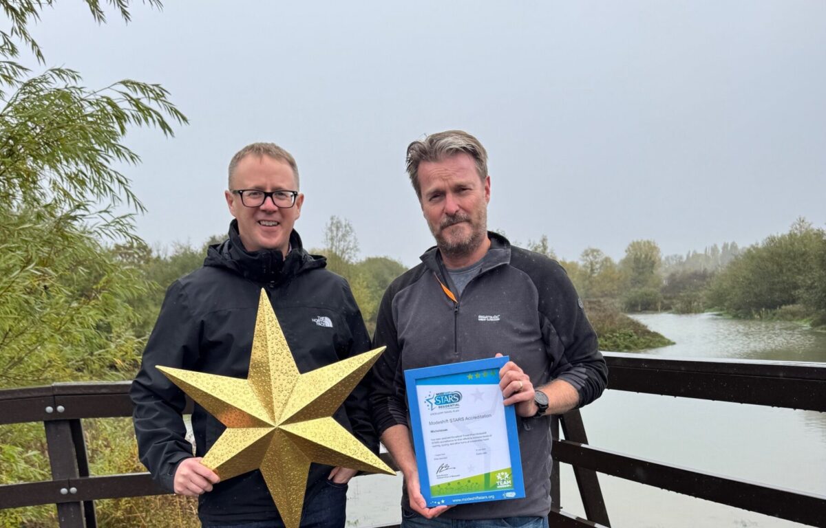 Two men stand side by side. One holds a Modeshift STARS Framed certificate, the other a large gold star.