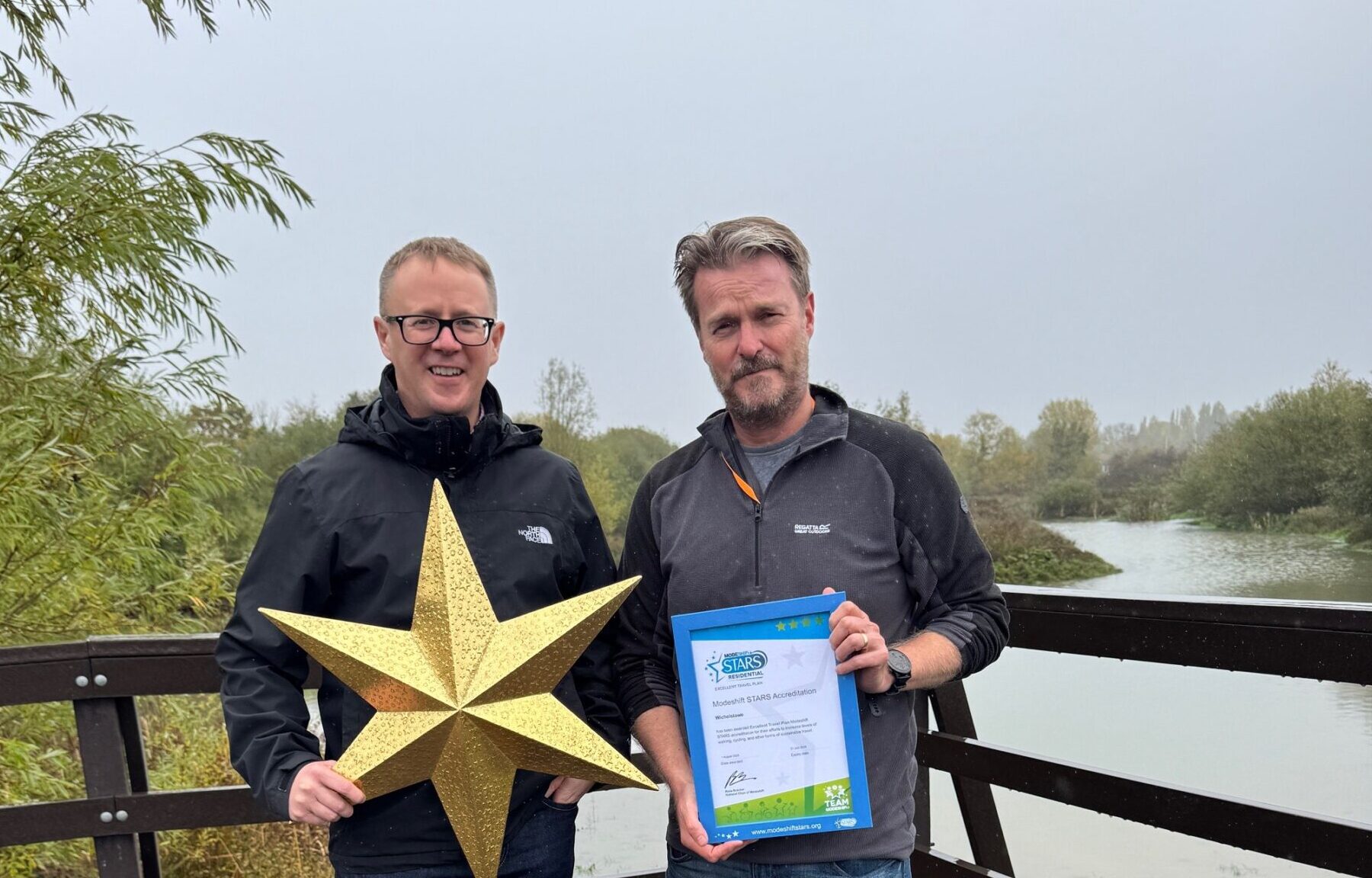 Two men stand side by side. One holds a Modeshift STARS Framed certificate, the other a large gold star.