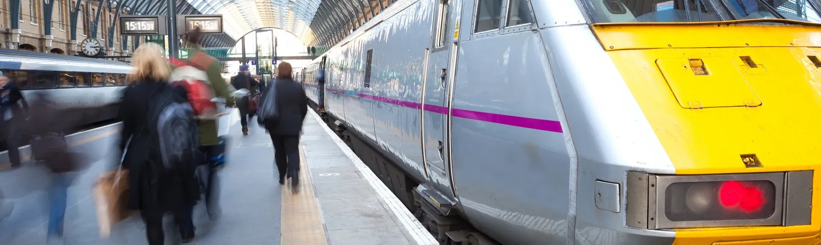 A railway platform. A train is stationery with people walking on the platform, they are blurred as is suspended in movement.